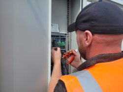 Technician working inside an industrial doors control cabinet, adjusting wiring and connections with orange tools and blue cables.