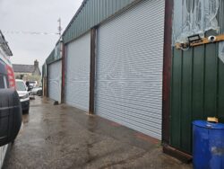 Industrial Roller Shutters at a warehouse entrance with large silver corrugated roller shutter doors, green cladding and automatic controls visible.