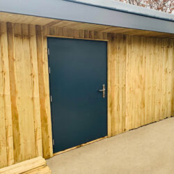 Grey steel security door set in a timber frame, with a dark surface finish and metal handle, for industrial and commercial steel doors.